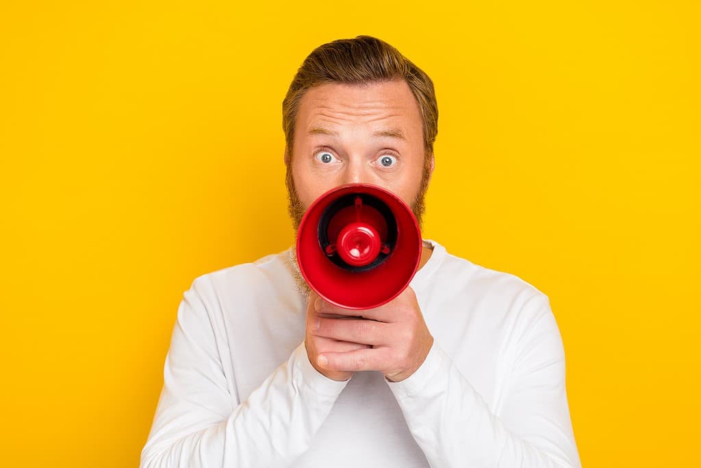 Photo portrait of nice young man hold megaphone announce shopping season promo wear stylish white look isolated on yellow color background.